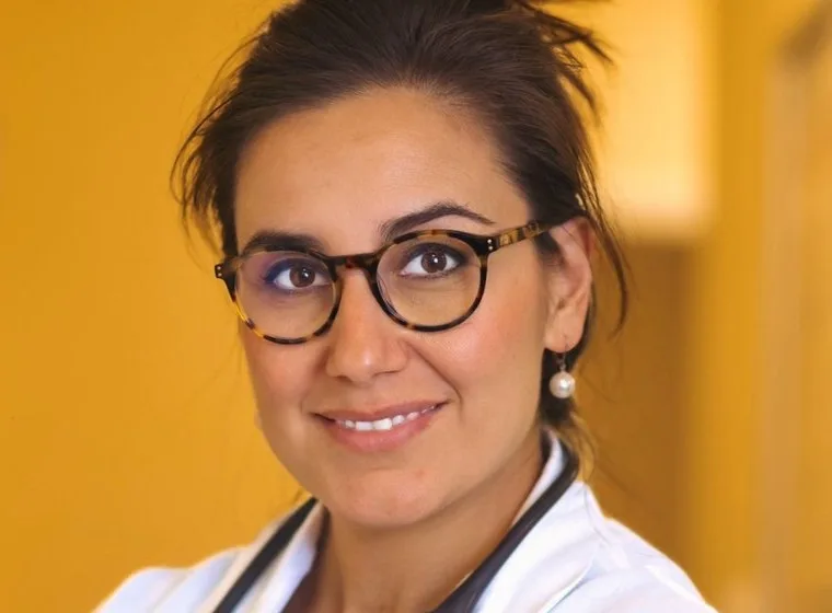 Reyhan Berkel, MD, arms folded, in front of the marigold wall of her office corridor.