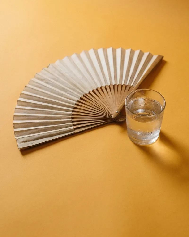 A paper hand fan beside a glass of water.