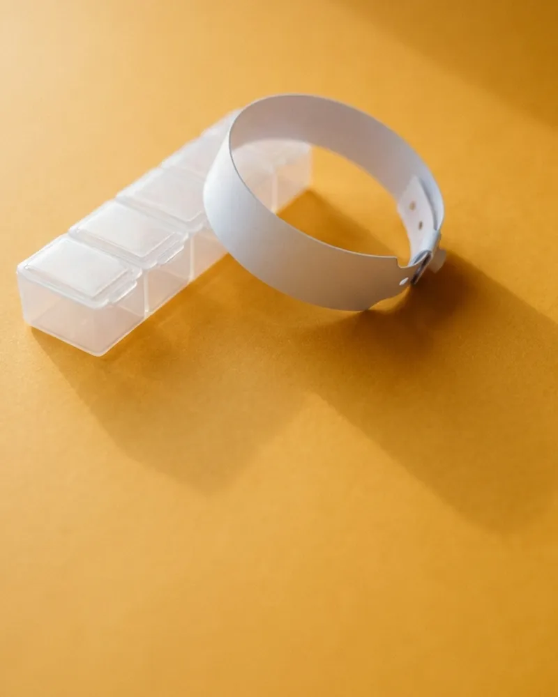 A cut hospital wristband beside a pill organizer.